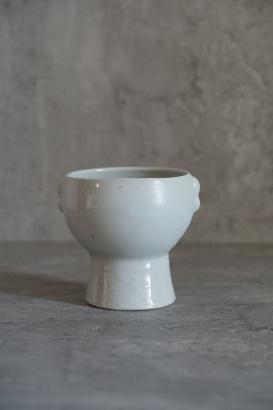 Tall white footed cup with rim lugs and a faint blue cast, on a pale grey ground.