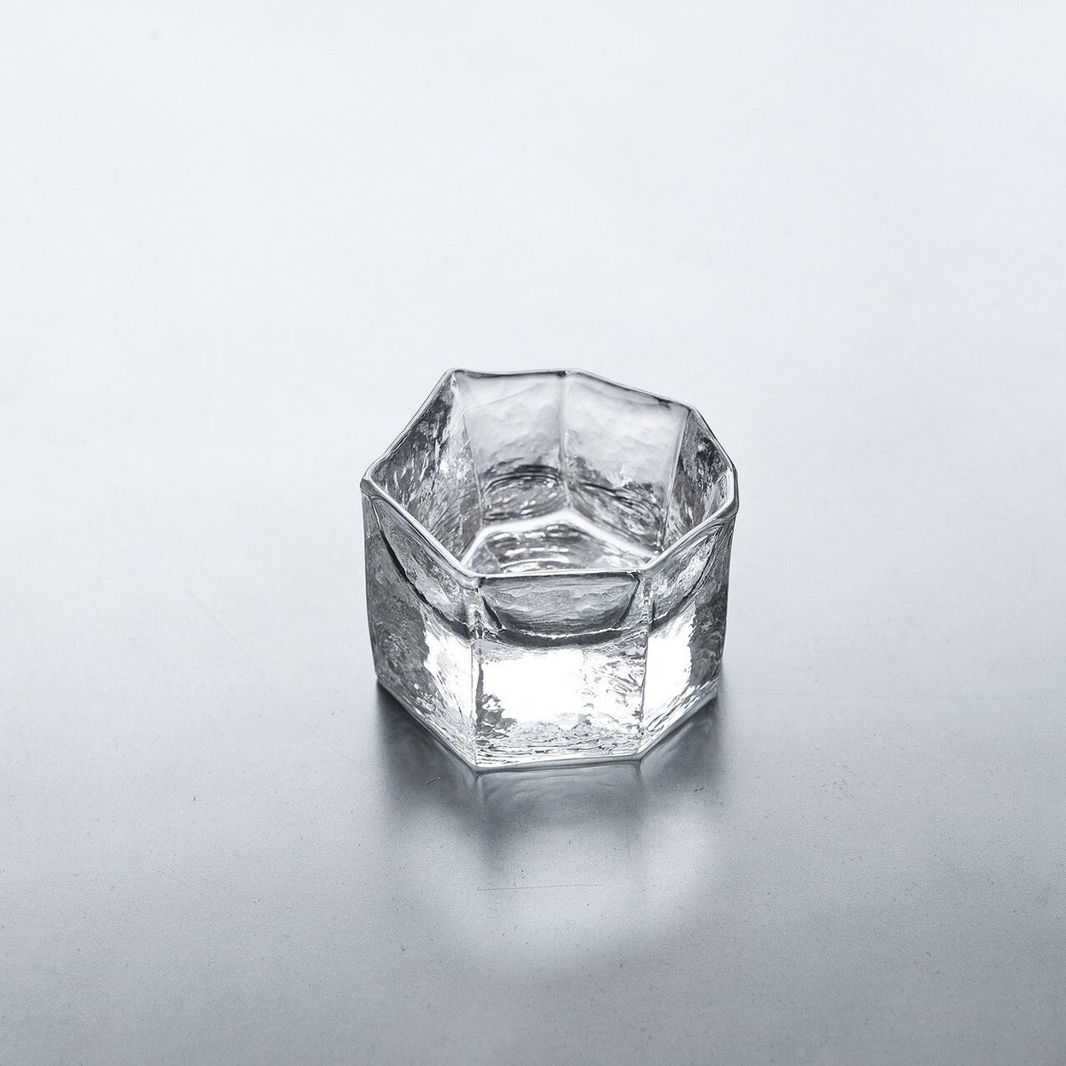 Low angular clear glass cup with heavy faceted sides catching bright highlights.