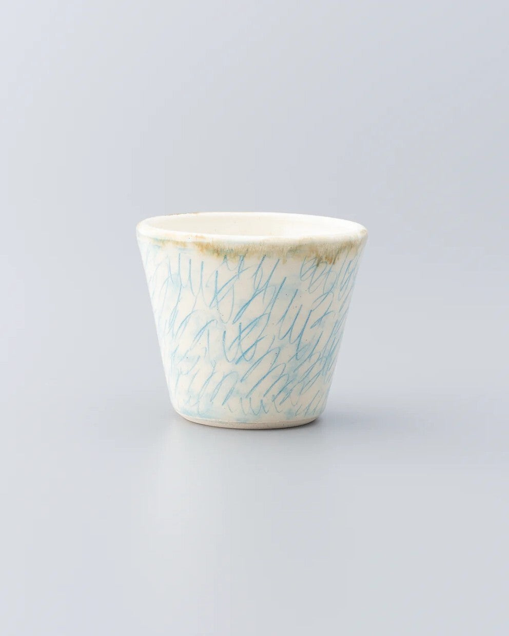Tapered cream ceramic cup hand-painted all over with fine pale blue brushstrokes.