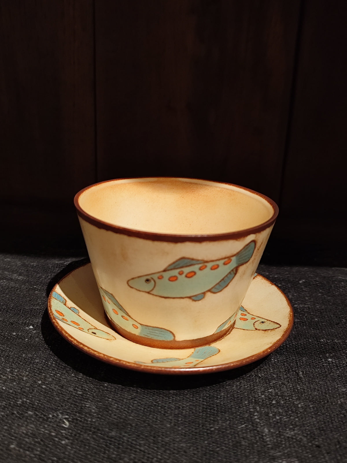 Cream cup and saucer with brown rims, painted with a pale blue whale swimming across the side.
