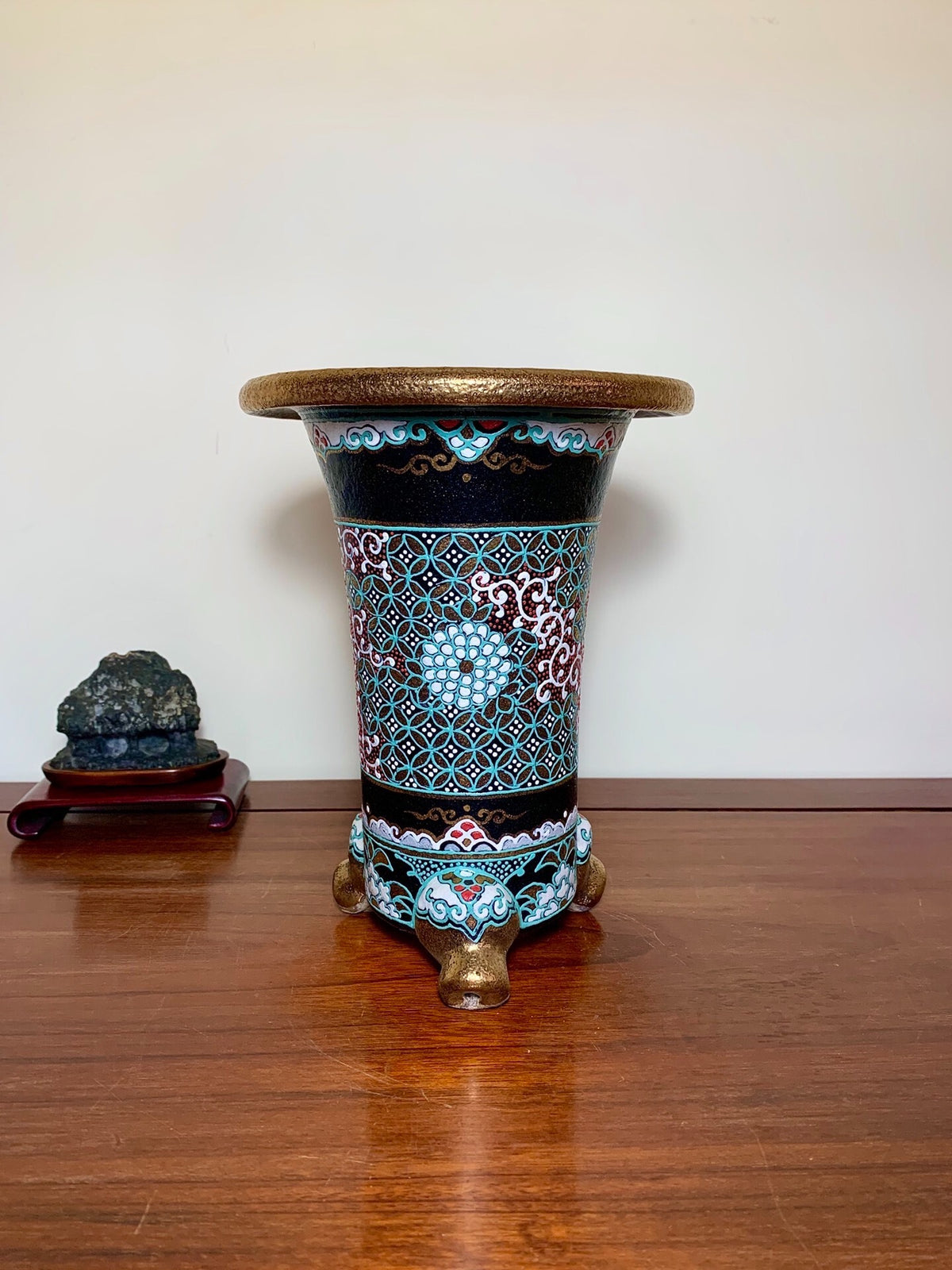 A tall, black glazed pot with turquoise and white floral patterns, resting on three lion-head feet.