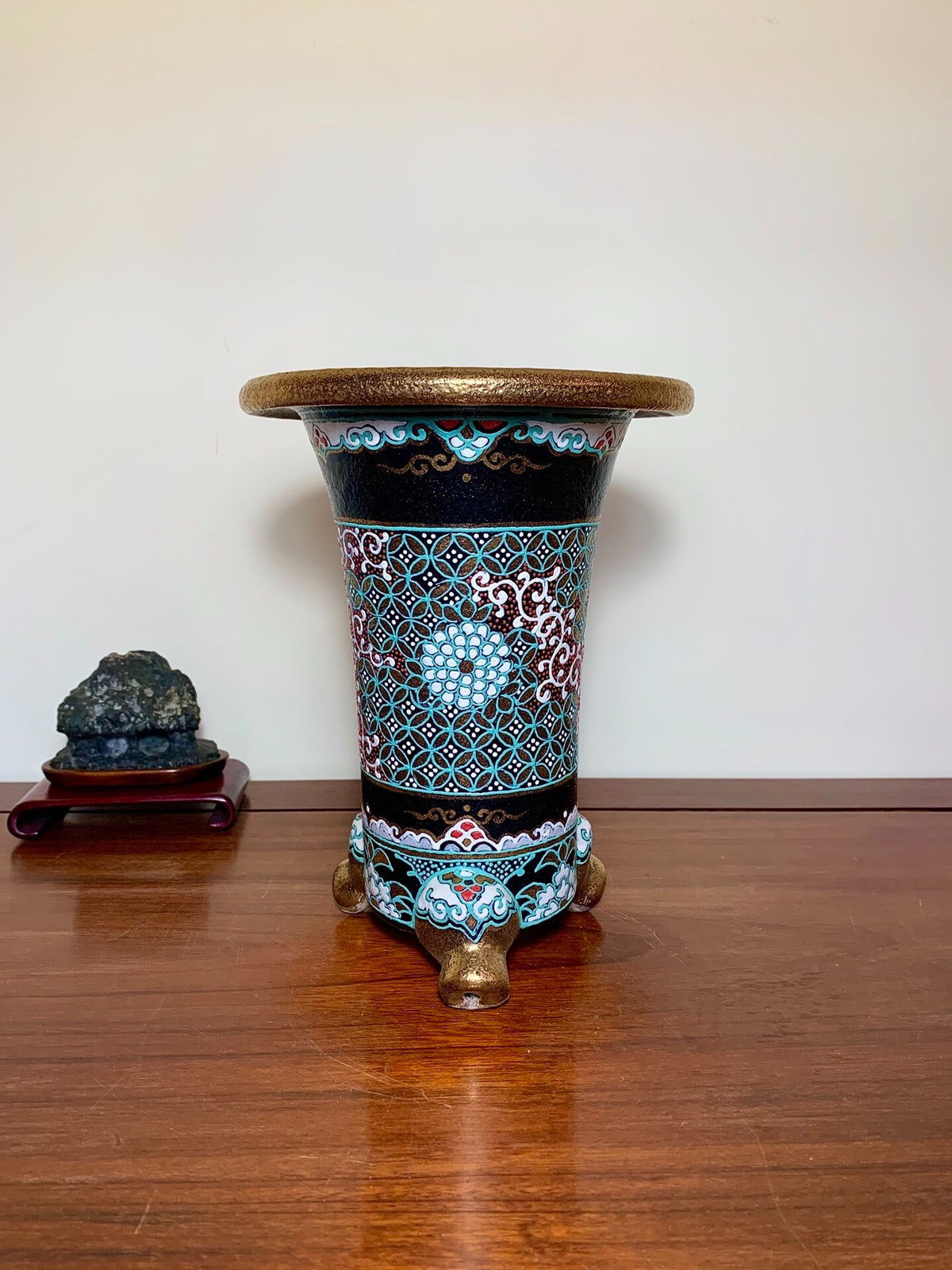 A tall, black glazed pot with turquoise and white floral patterns, resting on three lion-head feet.