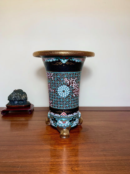 A tall, black glazed pot with turquoise and white floral patterns, resting on three lion-head feet.