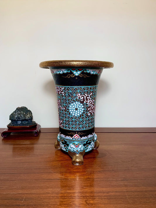 A tall, black glazed pot with turquoise and white floral patterns, resting on three lion-head feet.