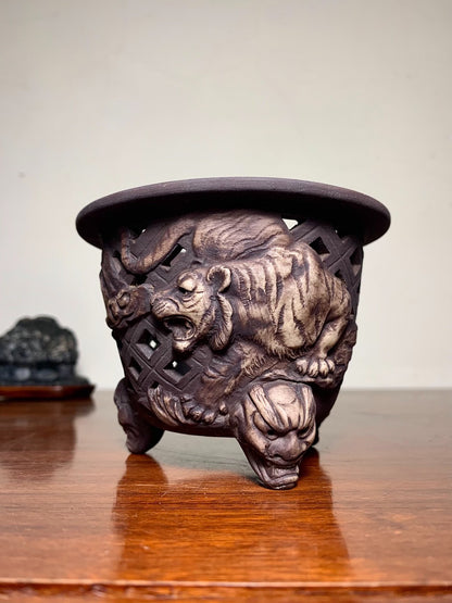 Dark brown glazed ceramic pot with three legs, featuring a carved tiger and lion in a lattice design.