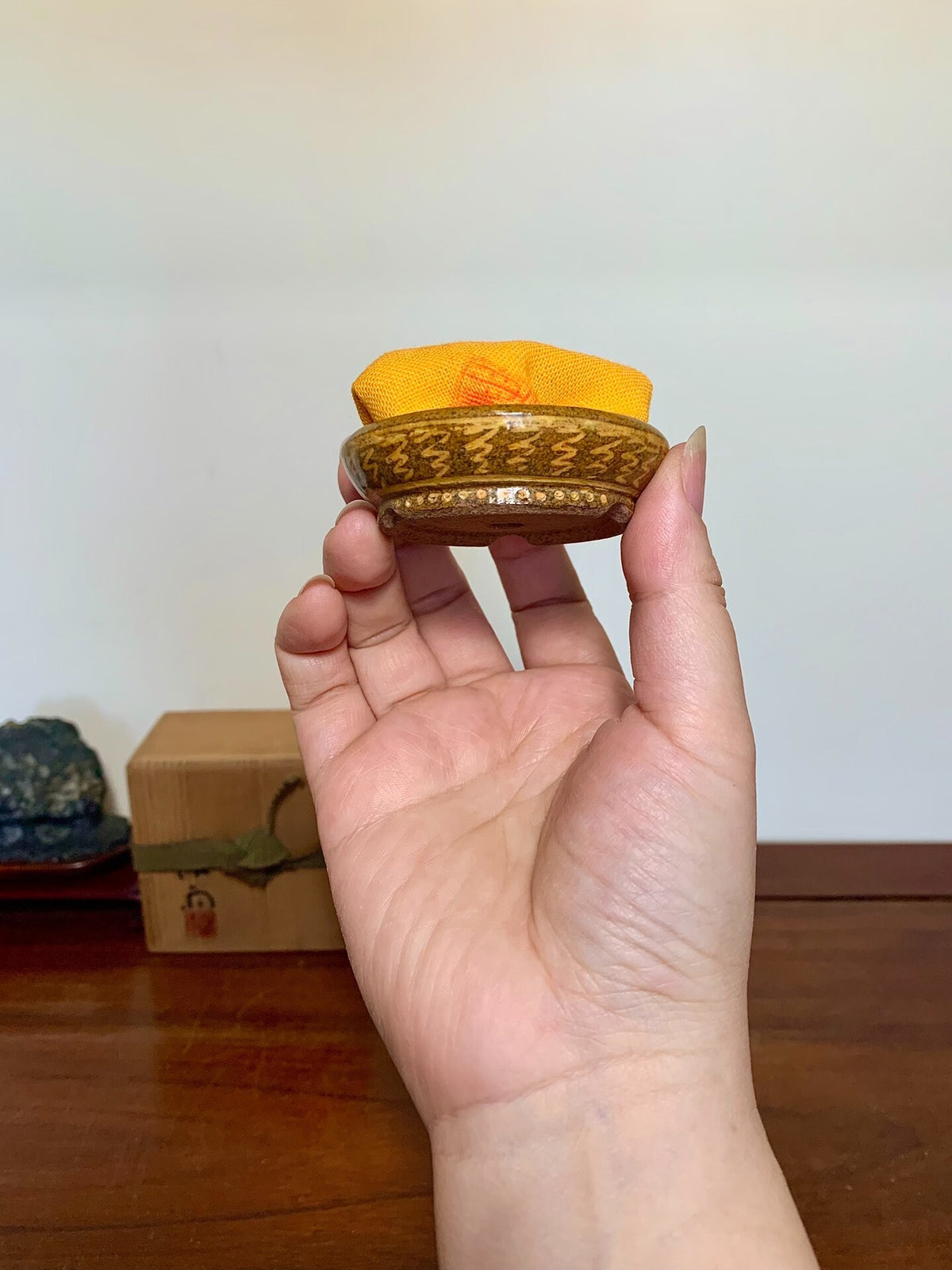 A small, round, gold-glazed pot with intricate engraved patterns, held in a hand.