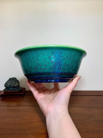 A hand holds a glossy, wide-rimmed pot with a green-to-blue gradient glaze and speckled texture.