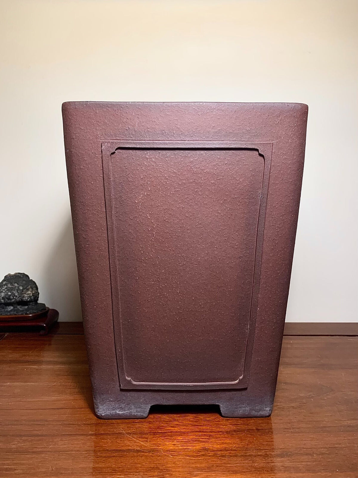 Dark brown matte rectangular pot with recessed panel, unglazed surface, sits on wooden floor.