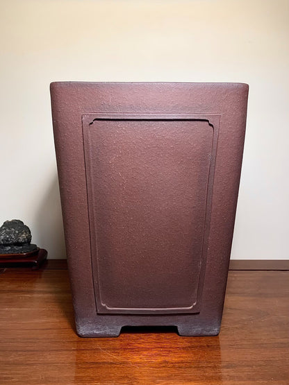 Dark brown matte rectangular pot with recessed panel, unglazed surface, sits on wooden floor.