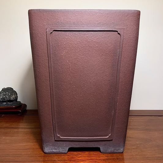 Dark brown matte rectangular pot with recessed panel, unglazed surface, sits on wooden floor.