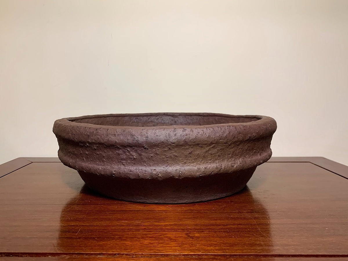 Dark brown, wide, shallow pot with textured, unglazed surface and thick rim.