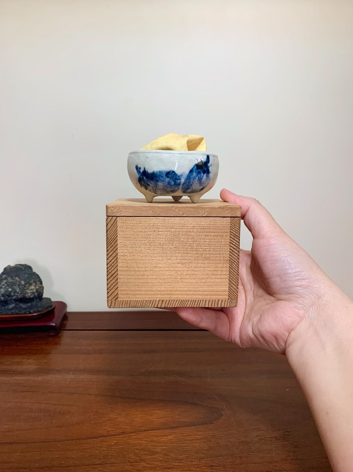 A hand holds a wooden box with a blue and white glazed ceramic bowl on top.
