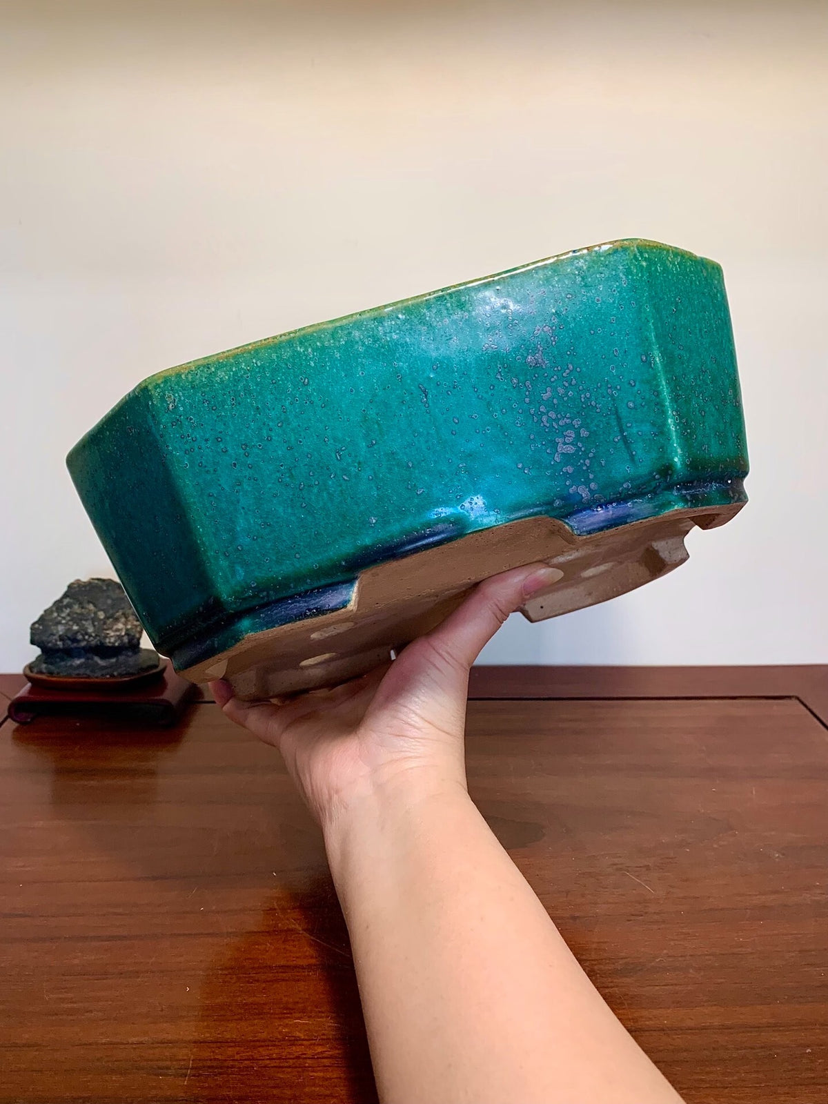 A hand holds a glossy, teal-glazed rectangular pot with a dark blue rim and unglazed base.