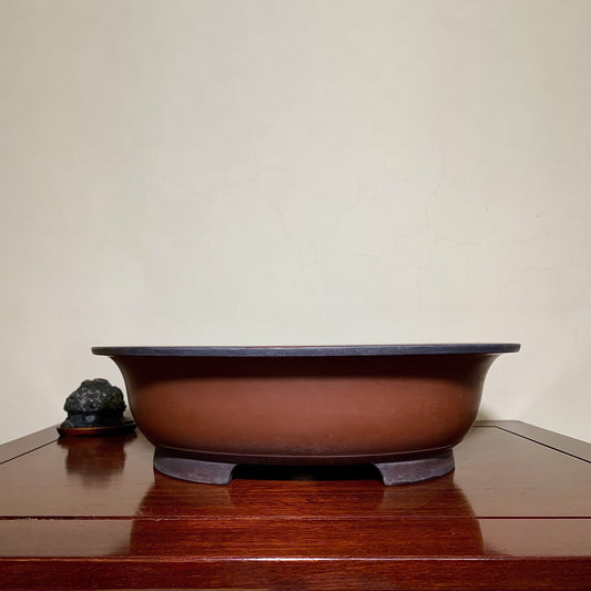 A glossy brown ceramic pot with a dark rim and three feet, beside a small dark rock.