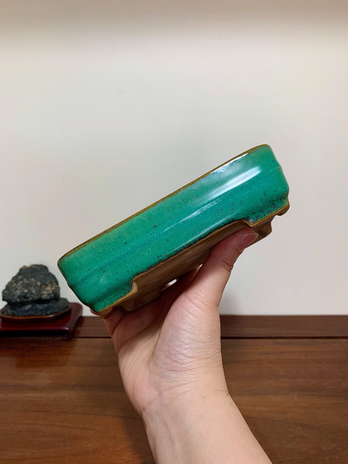 A hand holds a glossy, rectangular green glazed pot with a brown rim.