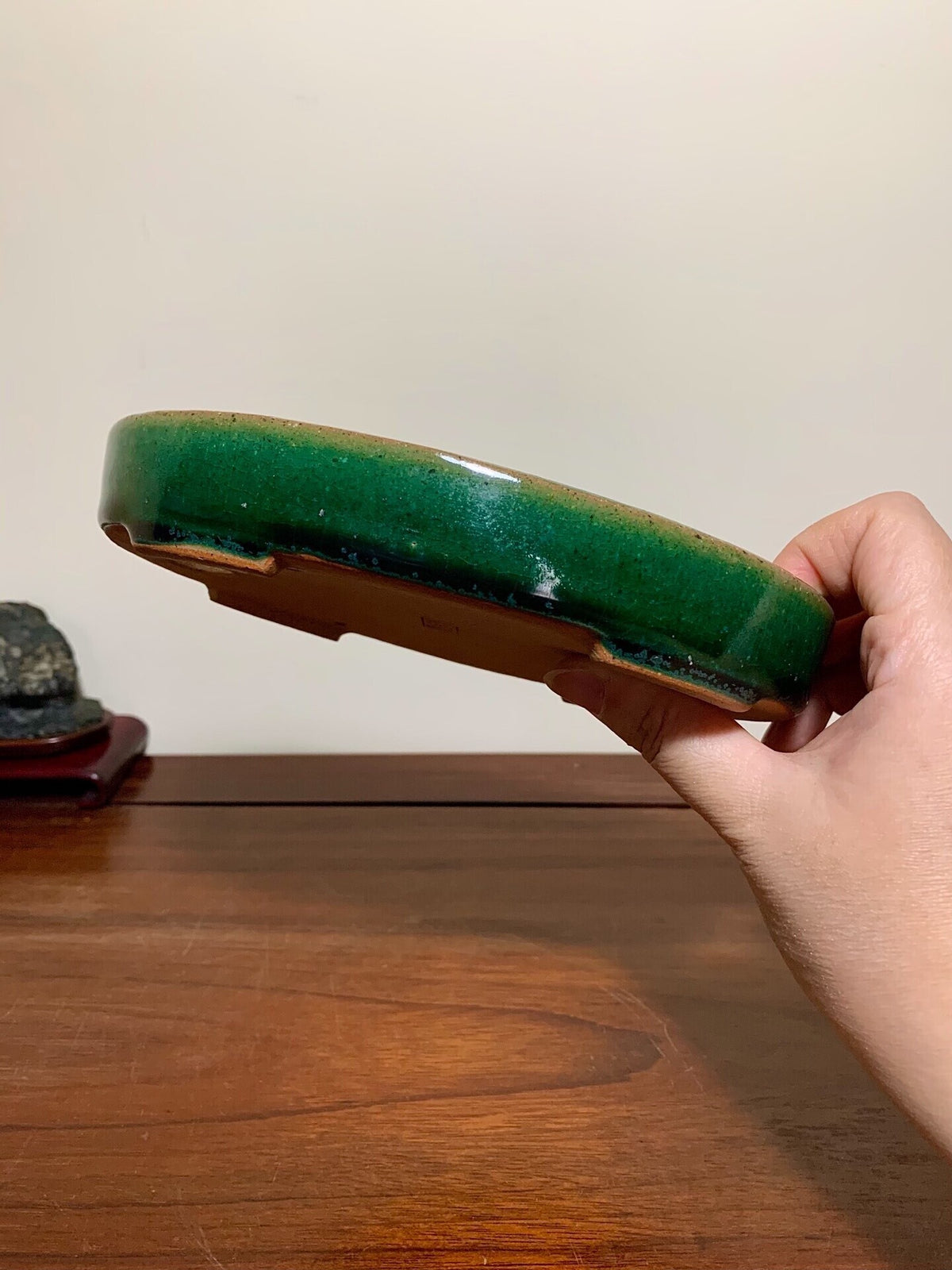 A hand holds a glossy, deep green glazed ceramic pot with a brown rim and unglazed base.
