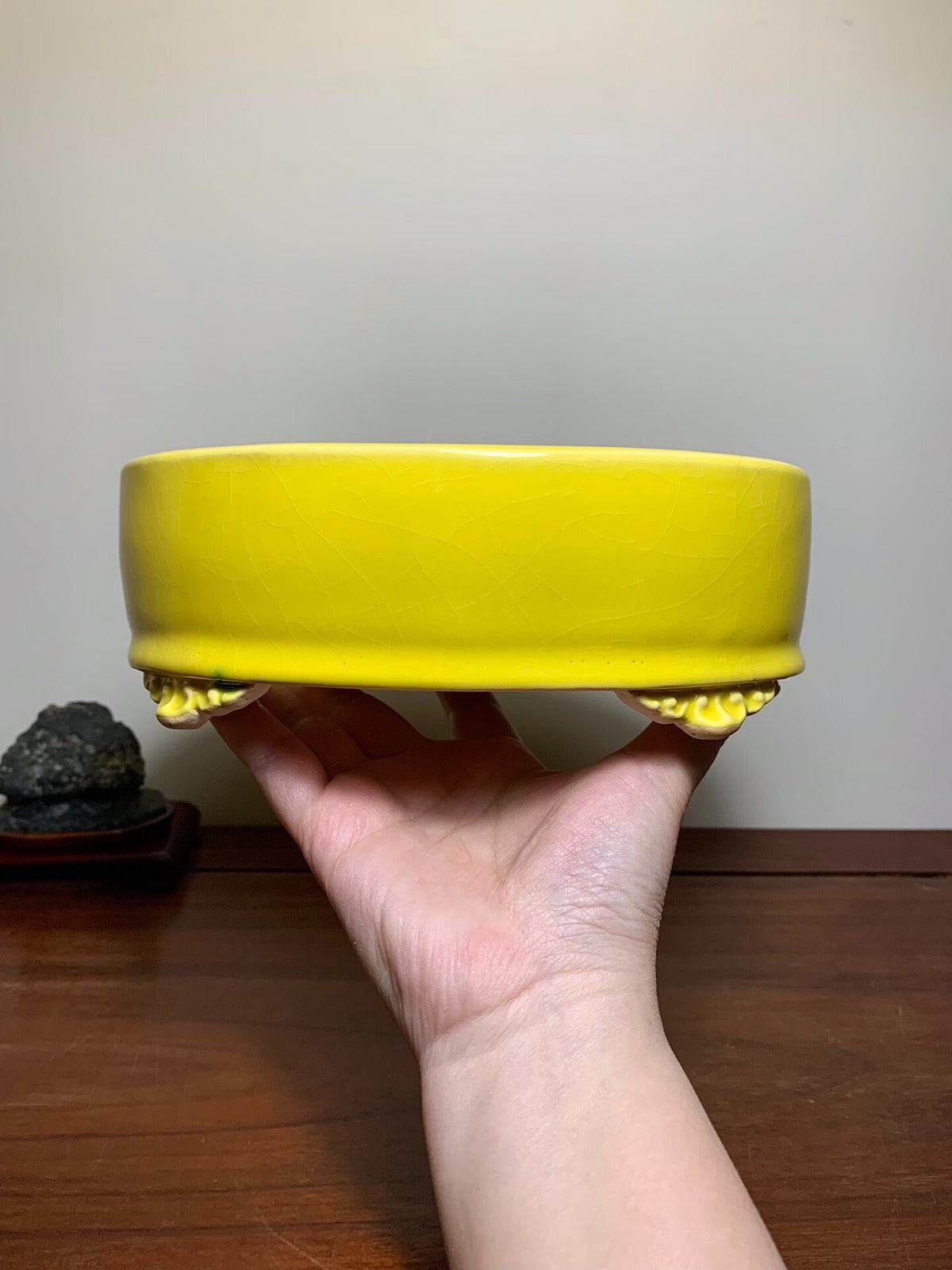 A hand holds a bright yellow glazed ceramic pot with scalloped footed base.