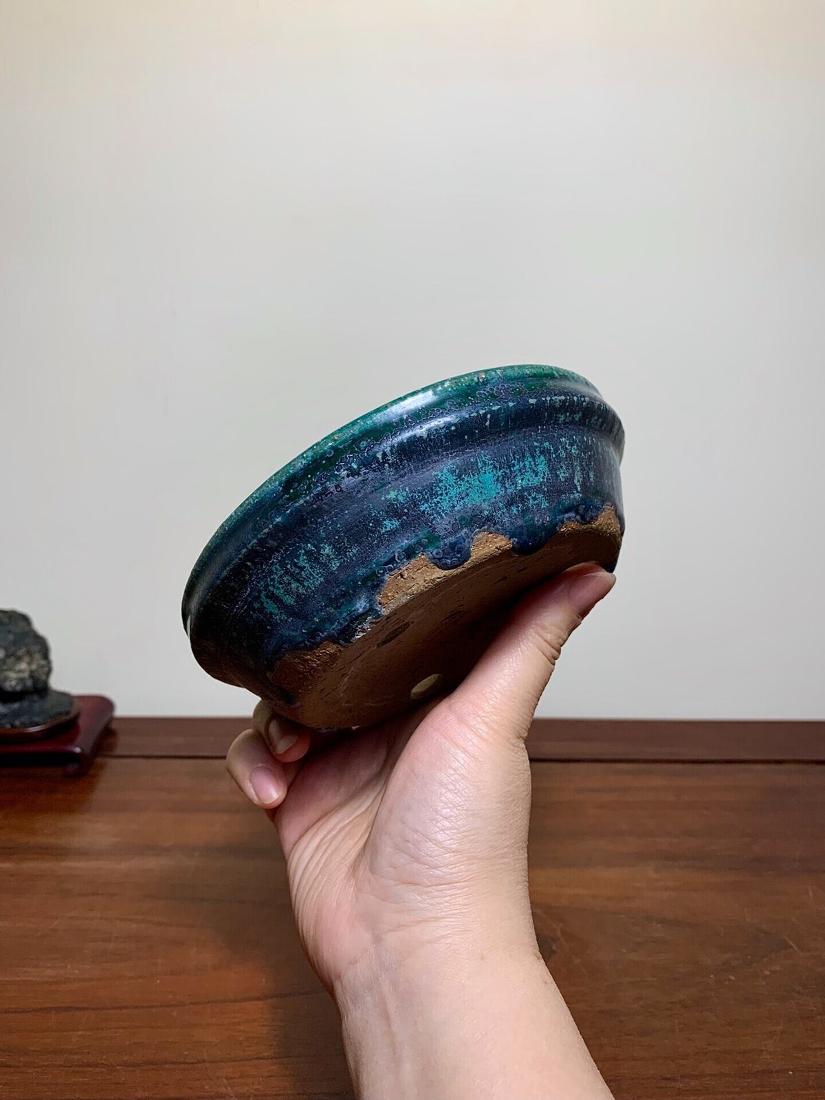 Hand holds small, round pot with glossy dark blue glaze and brown unglazed base.