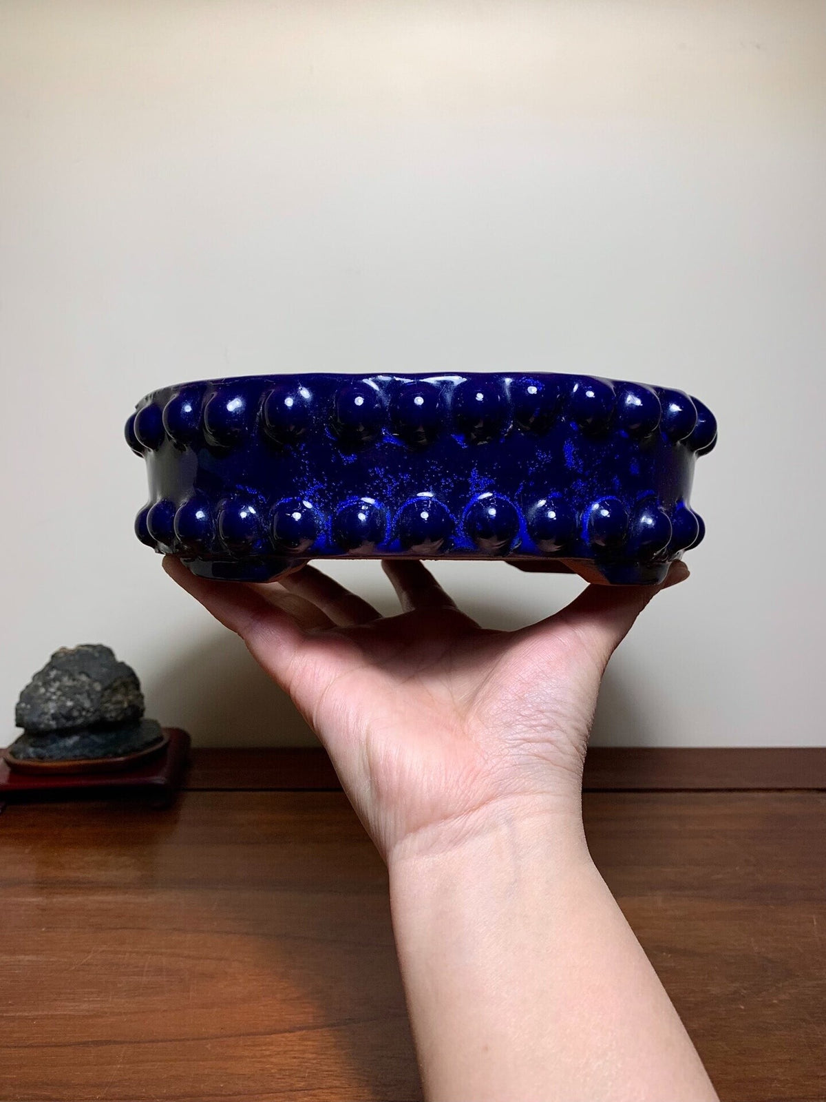 A hand holds a glossy, deep blue ceramic pot with raised, rounded knobs around its rim.