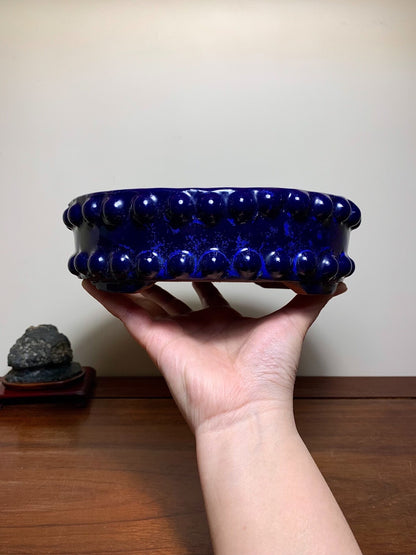 A hand holds a glossy, deep blue ceramic pot with raised, rounded knobs around its rim.