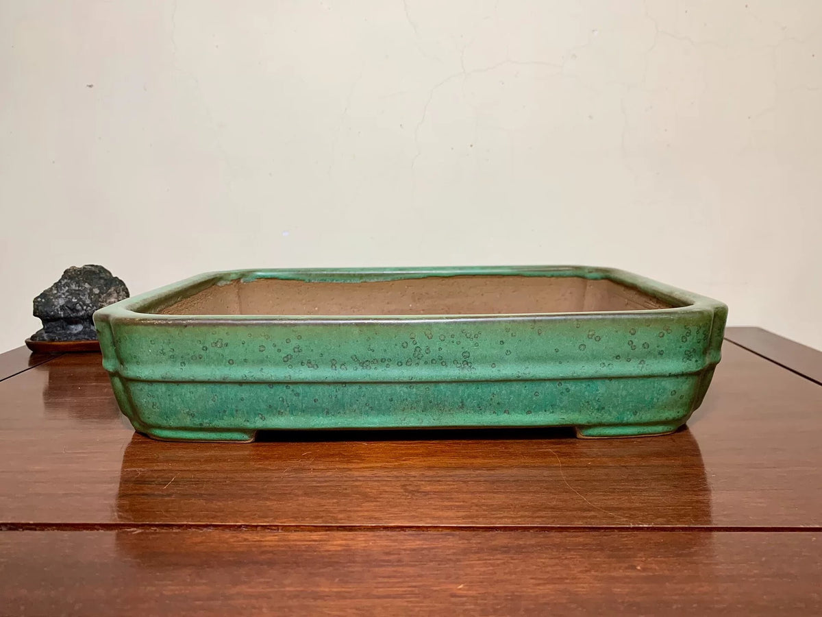 Rectangular green glazed pot with speckled surface, sits on wooden table.