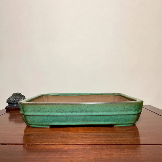 Rectangular green glazed pot with speckled surface, sits on wooden table.