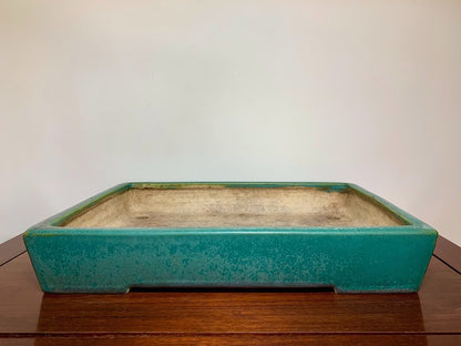 A rectangular glazed turquoise pot with a weathered interior sits on a wooden surface.