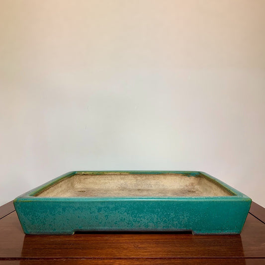 A rectangular glazed turquoise pot with a weathered interior sits on a wooden surface.
