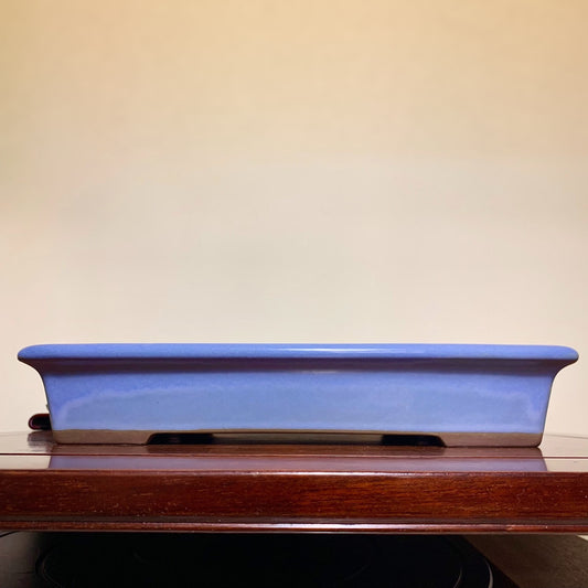 A glossy, rectangular blue glazed pot with a dark brown rim and two drainage holes.