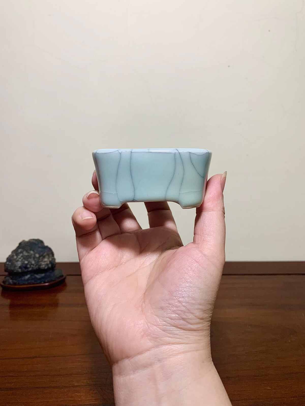 A hand holds a small, light blue glazed rectangular pot with visible crackle pattern.