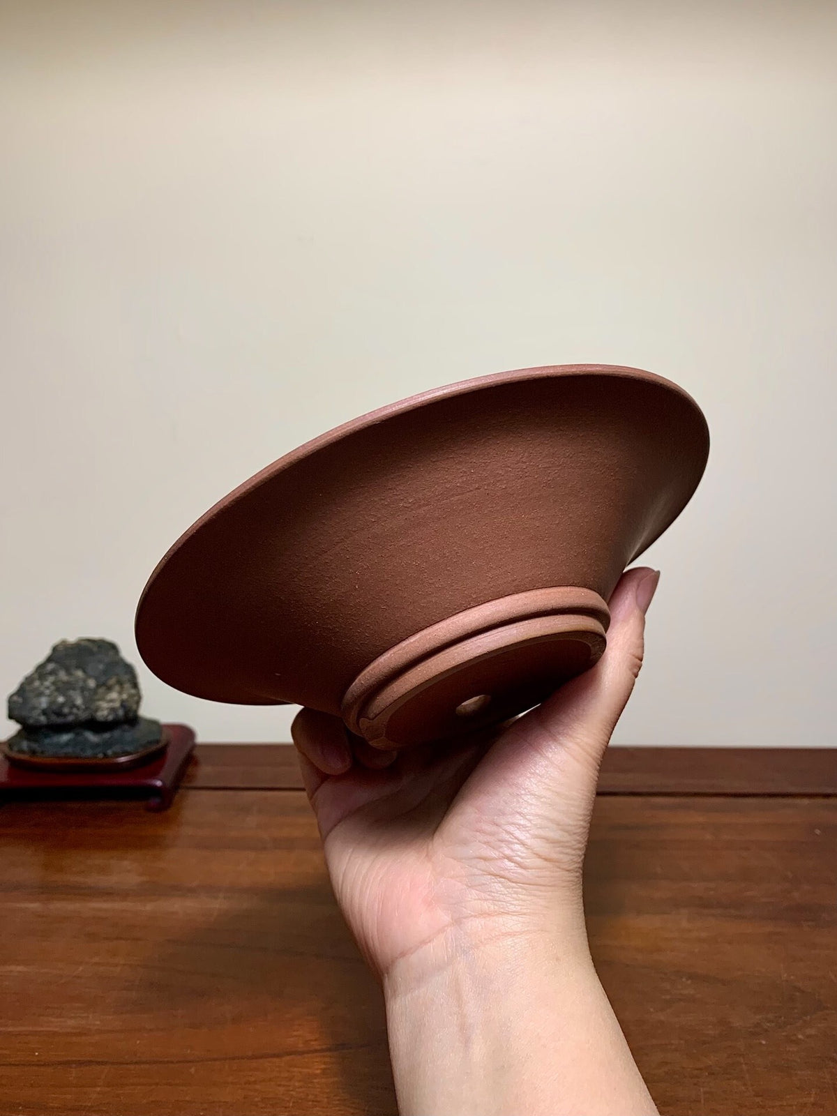 A hand holds a matte, reddish-brown ceramic bowl with a flared rim and unglazed base.