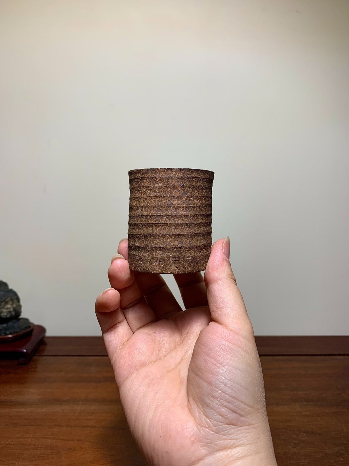 A hand holds a small, brown, ribbed ceramic pot with a matte finish.