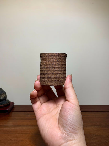 A hand holds a small, brown, ribbed ceramic pot with a matte finish.