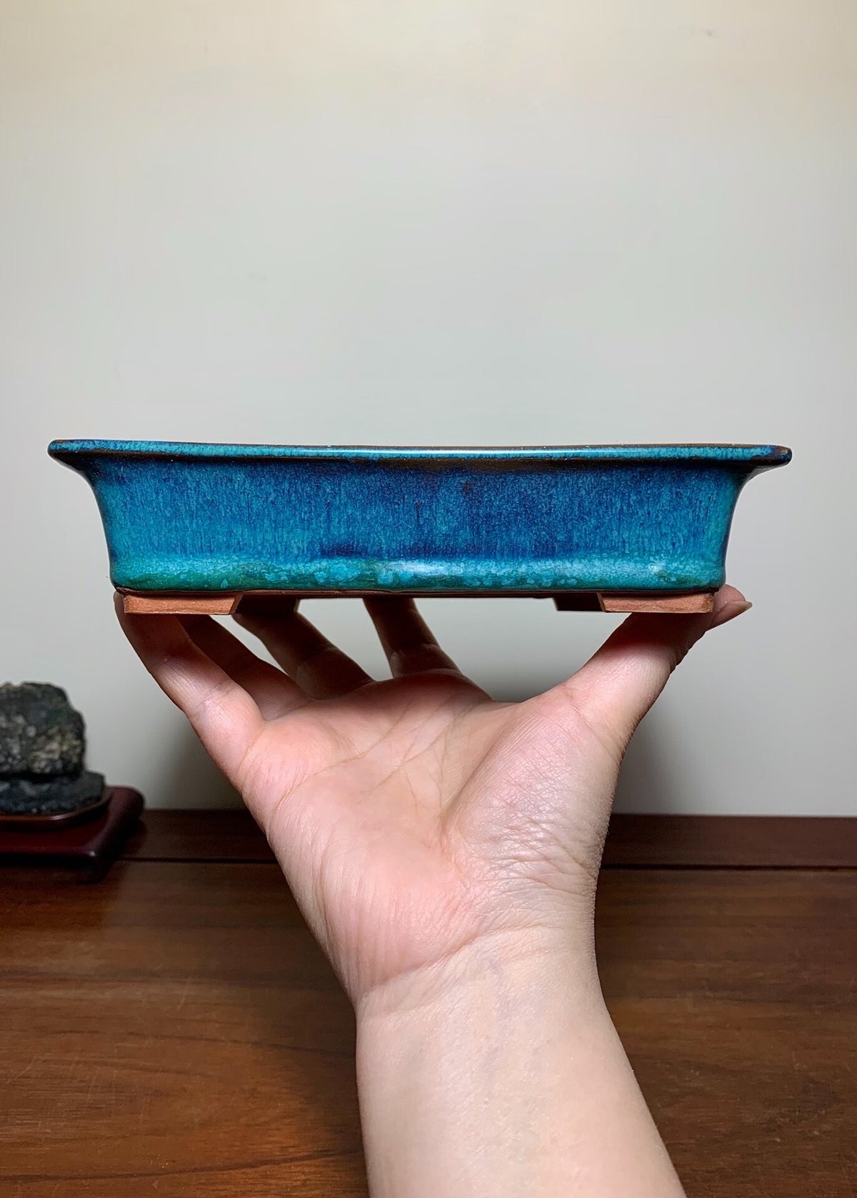 A hand holds a rectangular, glossy blue glazed pot with a textured surface and unglazed brown rim.