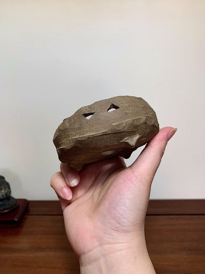 A hand holds a rough, brown, unglazed stone with two triangular holes.