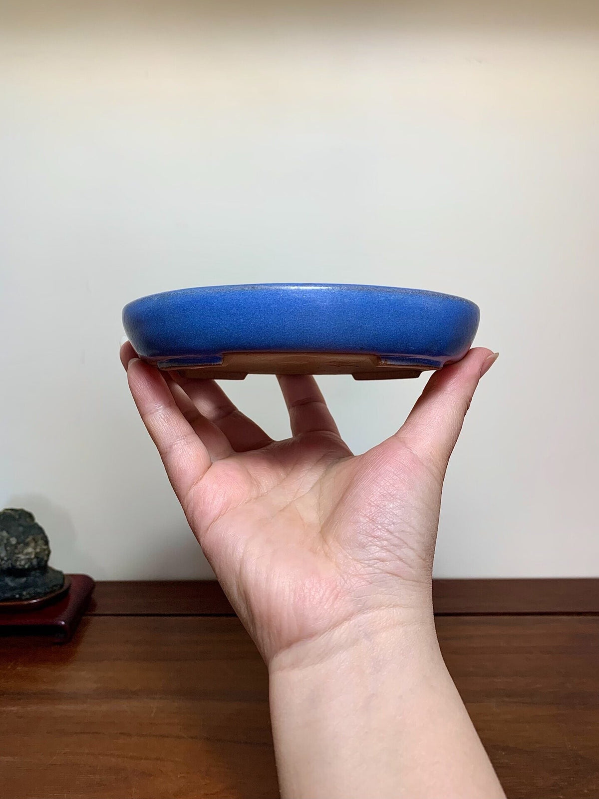 A hand holds a small, round, glossy blue glazed pot with a flat base.