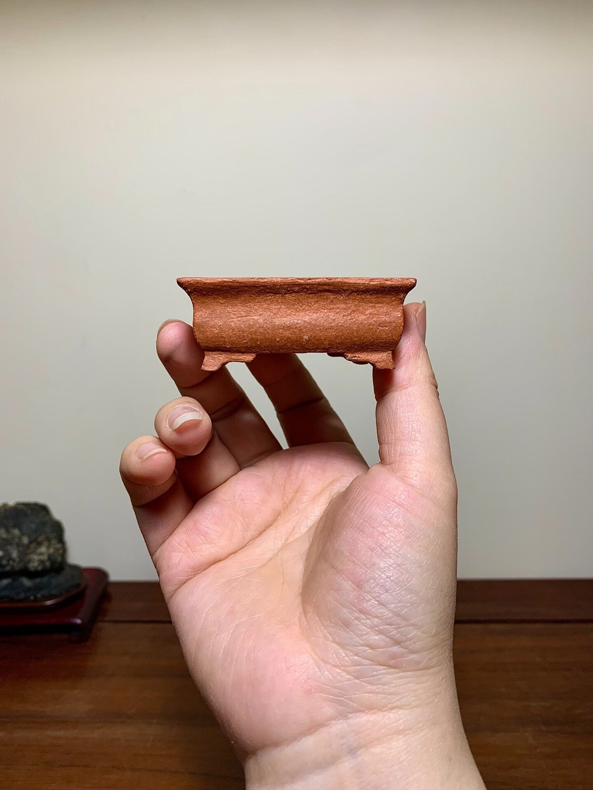 A small, unglazed terracotta pot with a rectangular rim and low sides, held in a hand.
