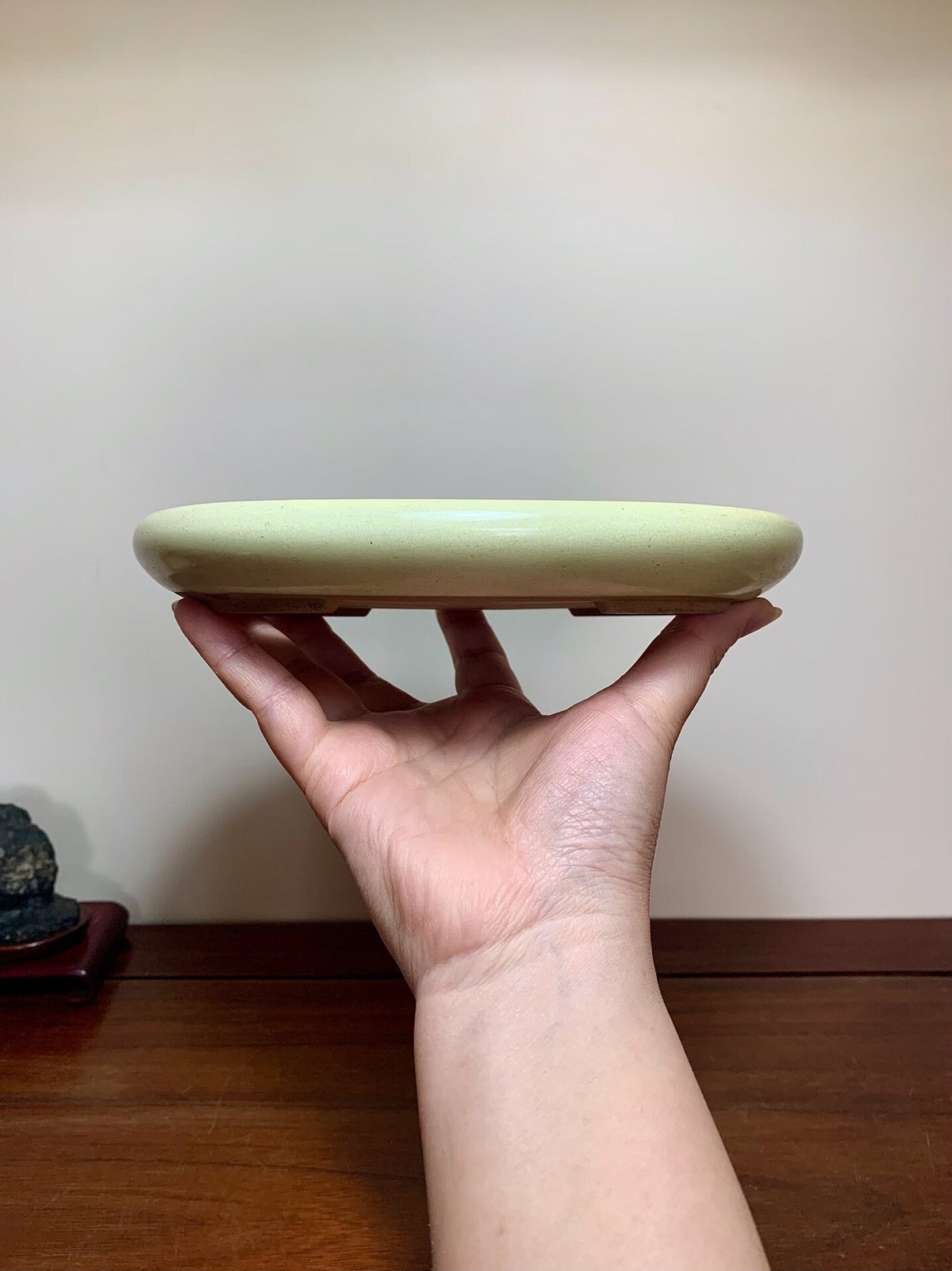 A hand holds a shallow, pale green glazed pot with a smooth, rounded rim.