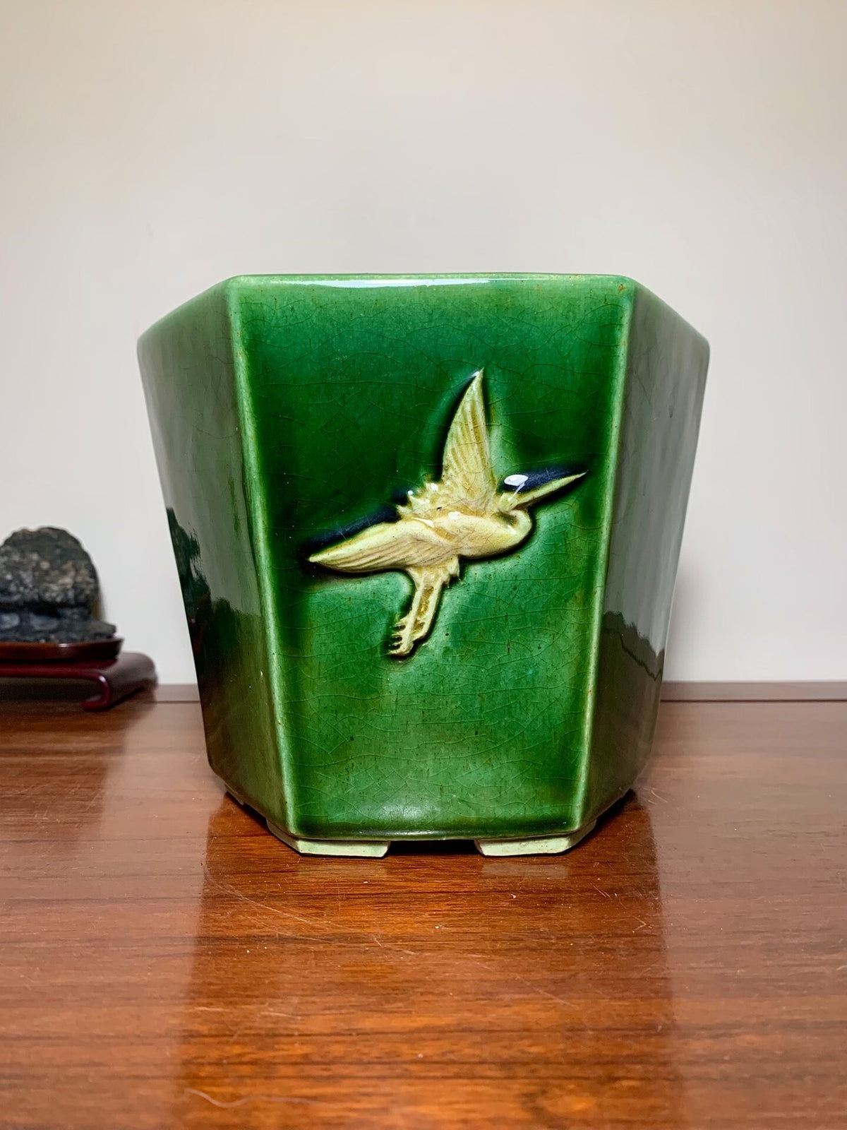 A glossy green hexagonal pot with a raised gold bird decoration.