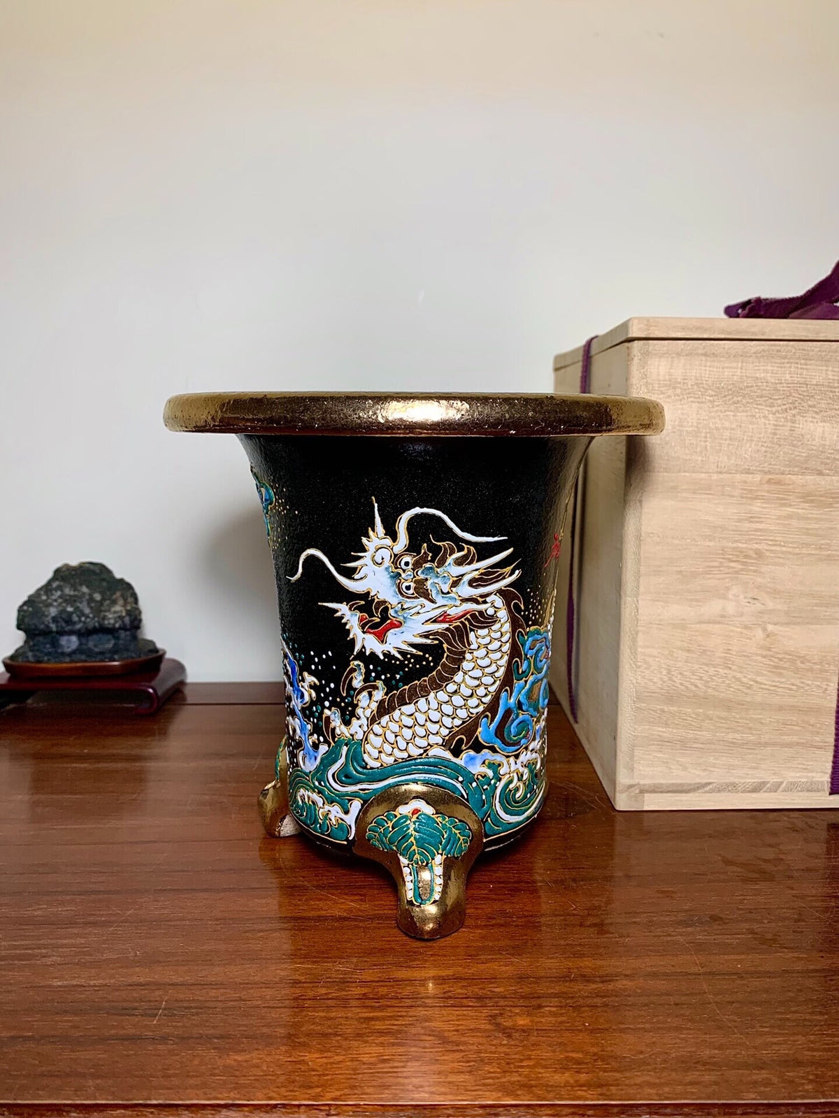 Black glazed pot with a white and gold dragon on a blue wave, three bronze feet.