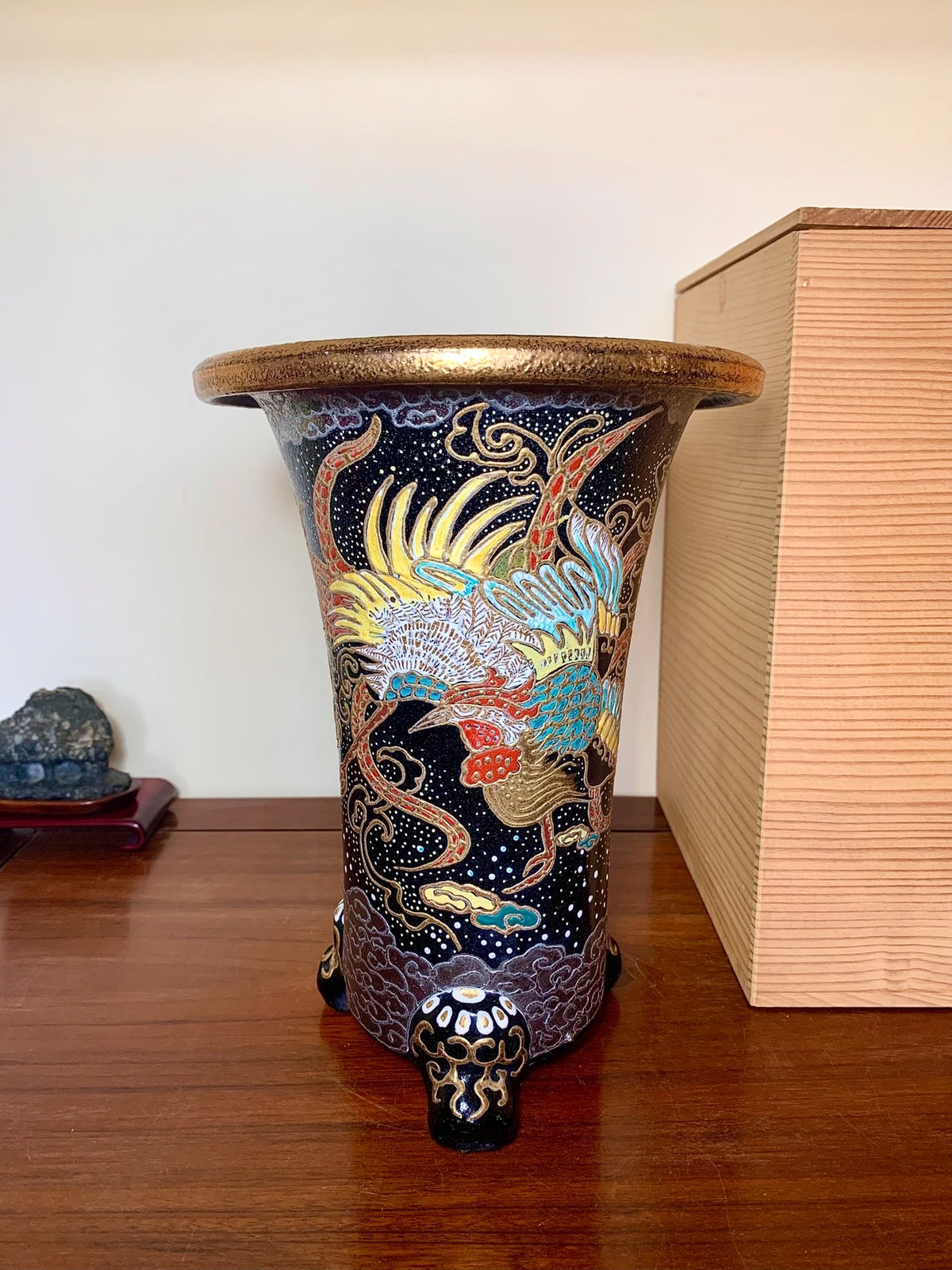 A tall, dark blue glazed pot with a golden rim, featuring a colorful phoenix design and three ornate feet.