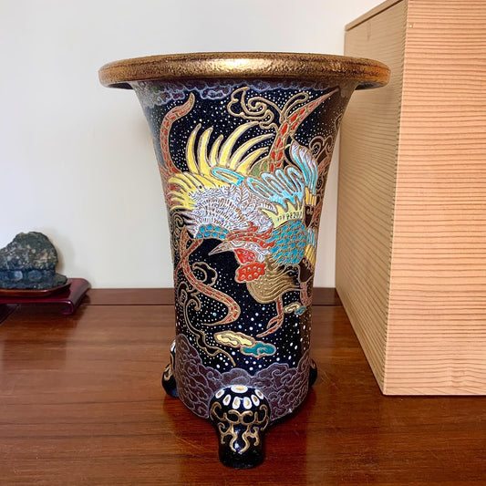 A tall, dark blue glazed pot with a golden rim, featuring a colorful phoenix design and three ornate feet.