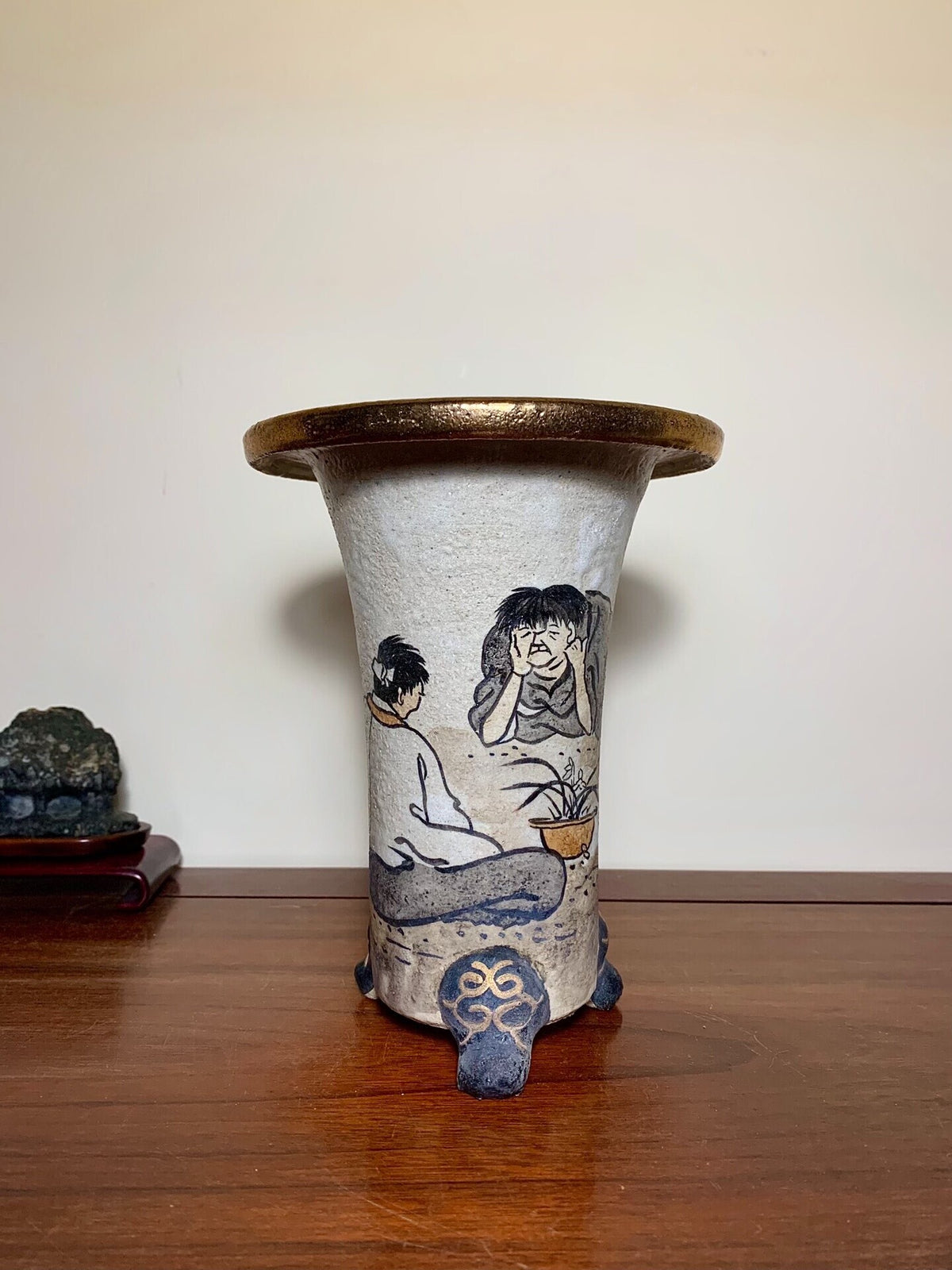 A tall, flared ceramic pot with matte grey glaze, hand-painted figures and a gold rim.