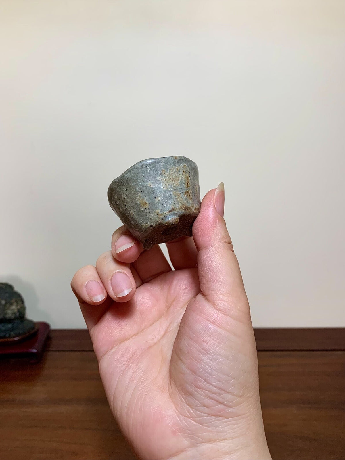A hand holds a small, grey, unglazed ceramic cup with a rough, speckled surface.