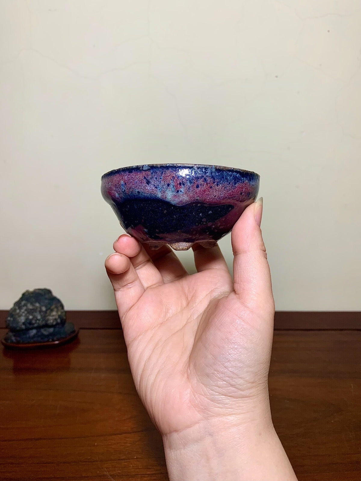 A hand holds a small, glossy bowl with a swirling dark blue and purple glaze.