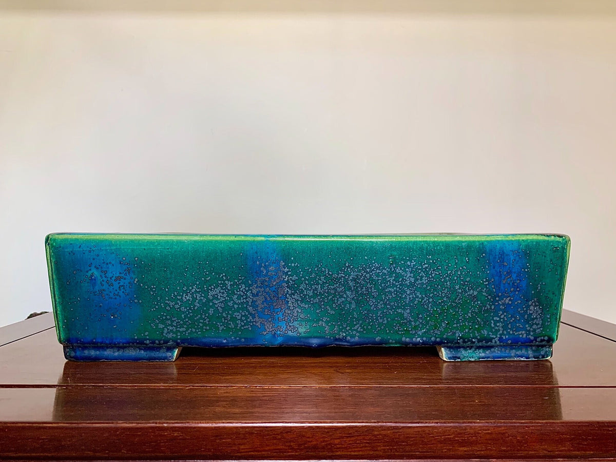 Rectangular glazed pot with speckled green and blue glaze, resting on wooden surface.