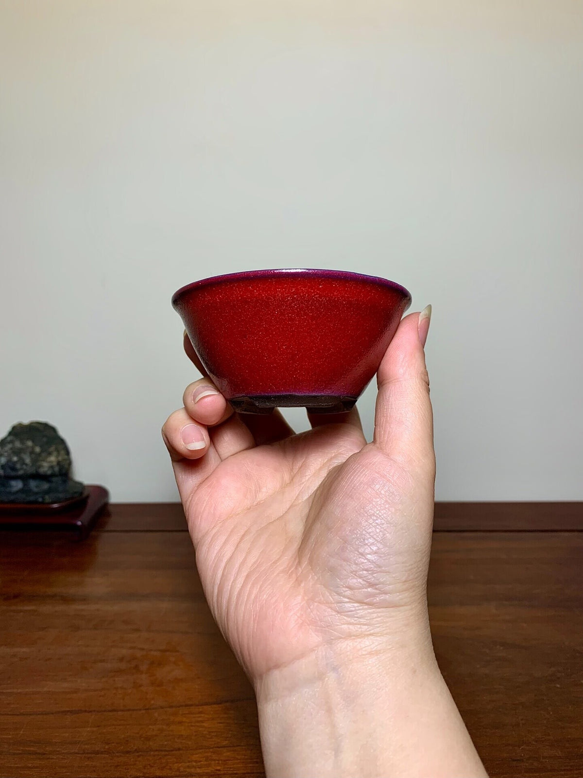 A hand holds a small, deep red, glossy ceramic bowl with a purple rim.