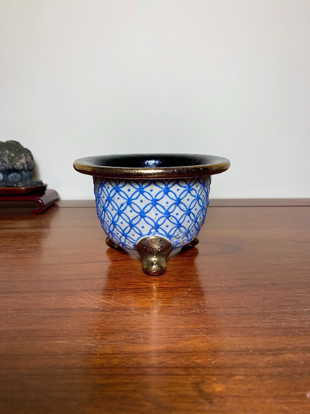A small, round ceramic pot with a blue geometric pattern and three bronze-colored feet.