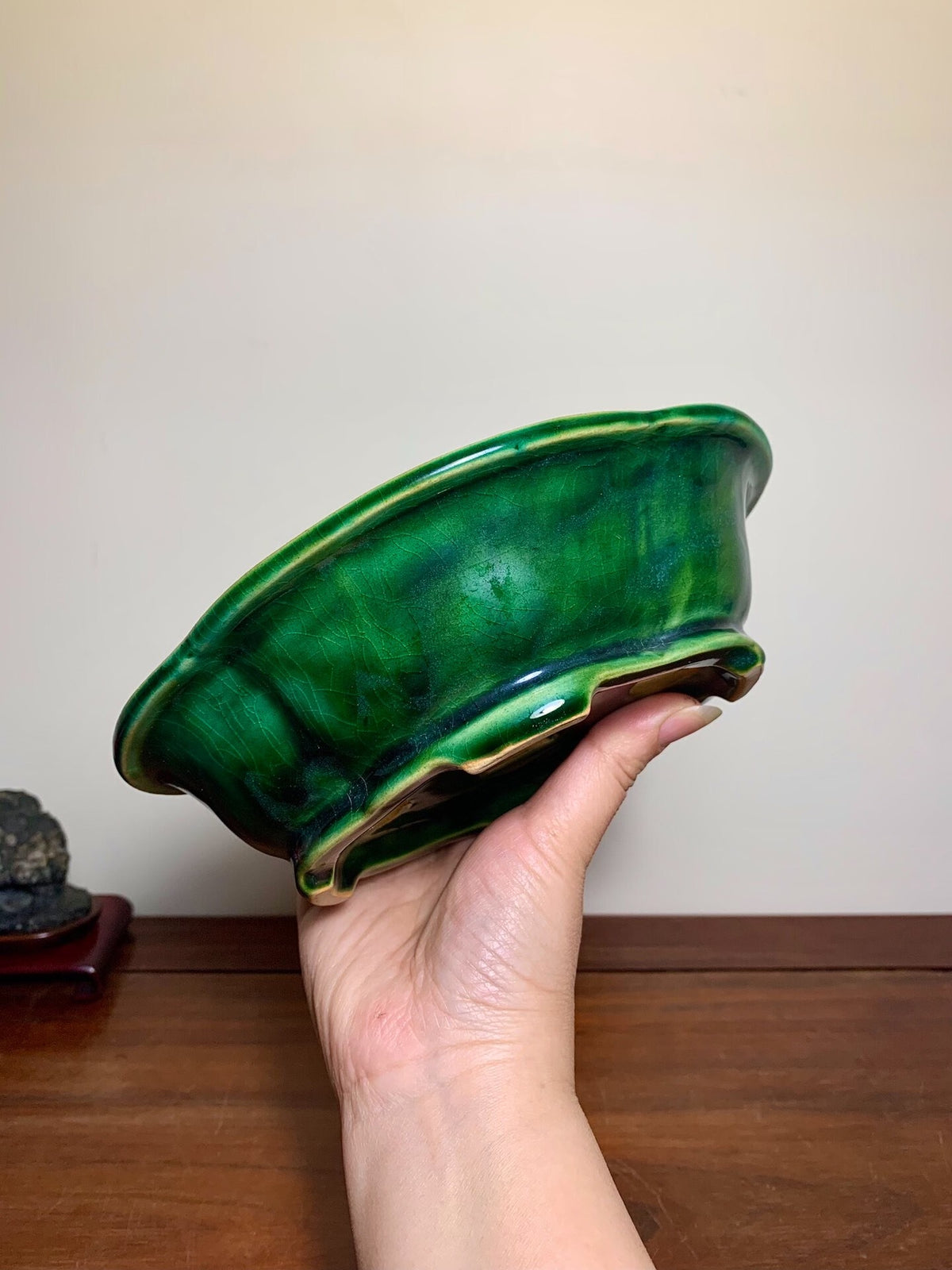 A hand holds a glossy, deep green glazed ceramic pot with a flared rim and scalloped edge.