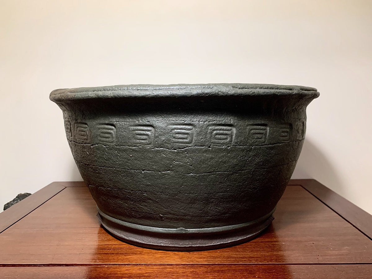 Dark grey unglazed ceramic pot with repeating geometric relief pattern around its midsection.